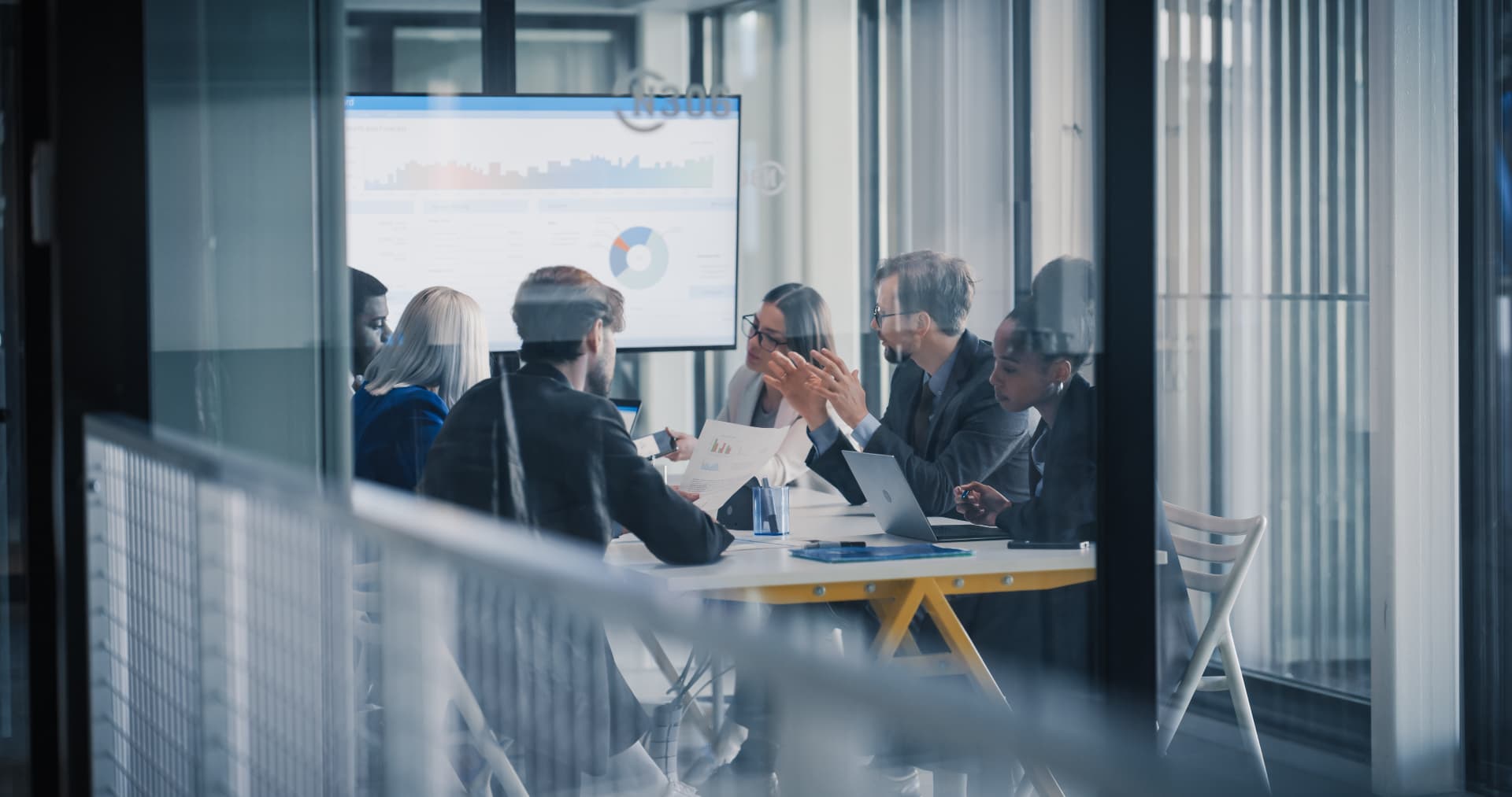 Business professionals in a meeting around a conference table with a data dashboard