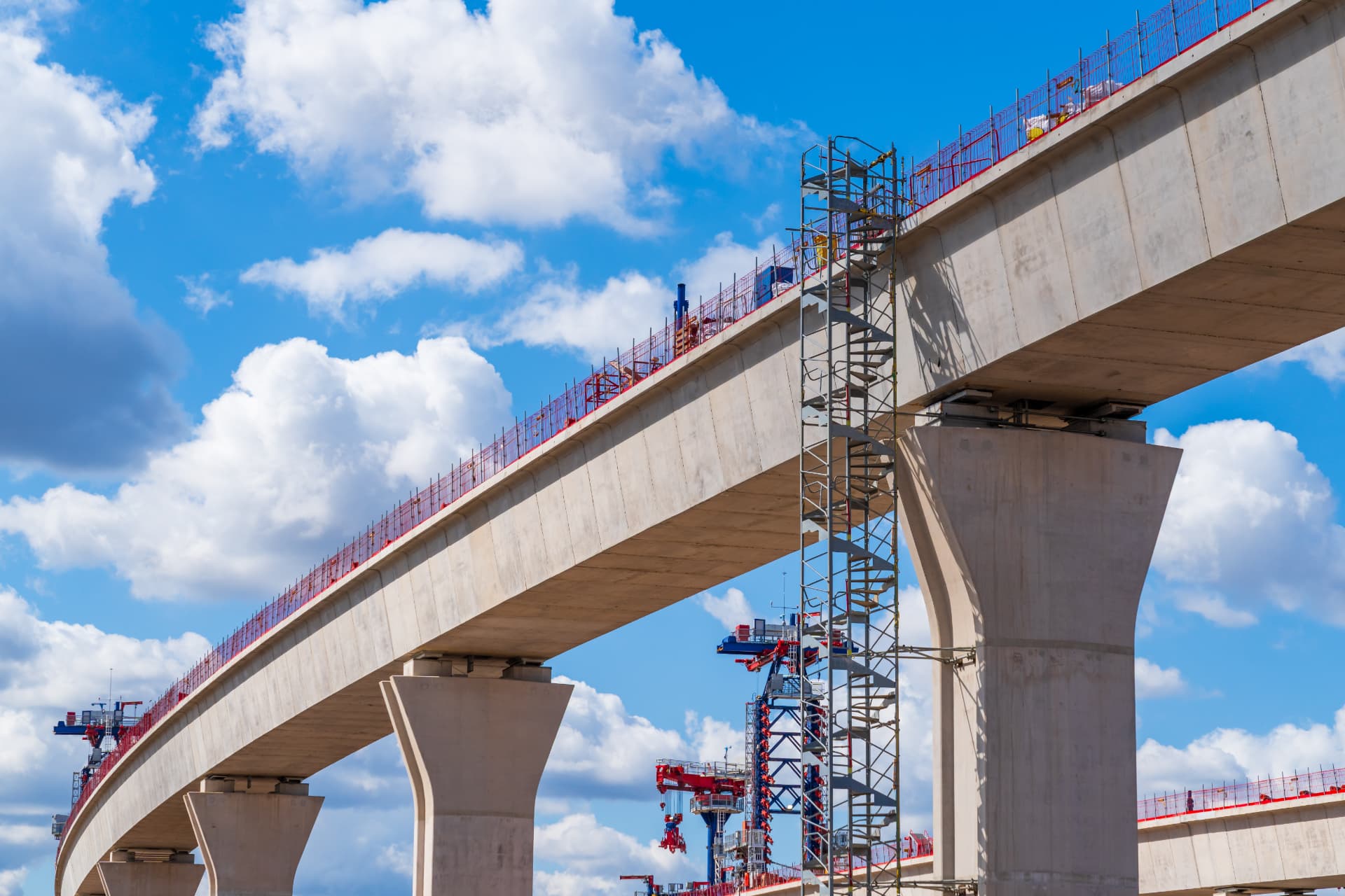 Elevated concrete transit viaduct under construction with scaffolding and cranes